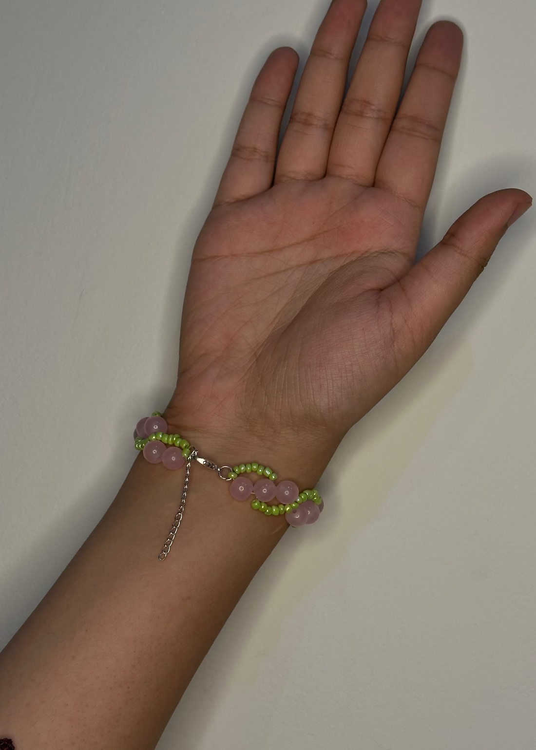 Hand wearing a bracelet with pink and green beads on a plain background
