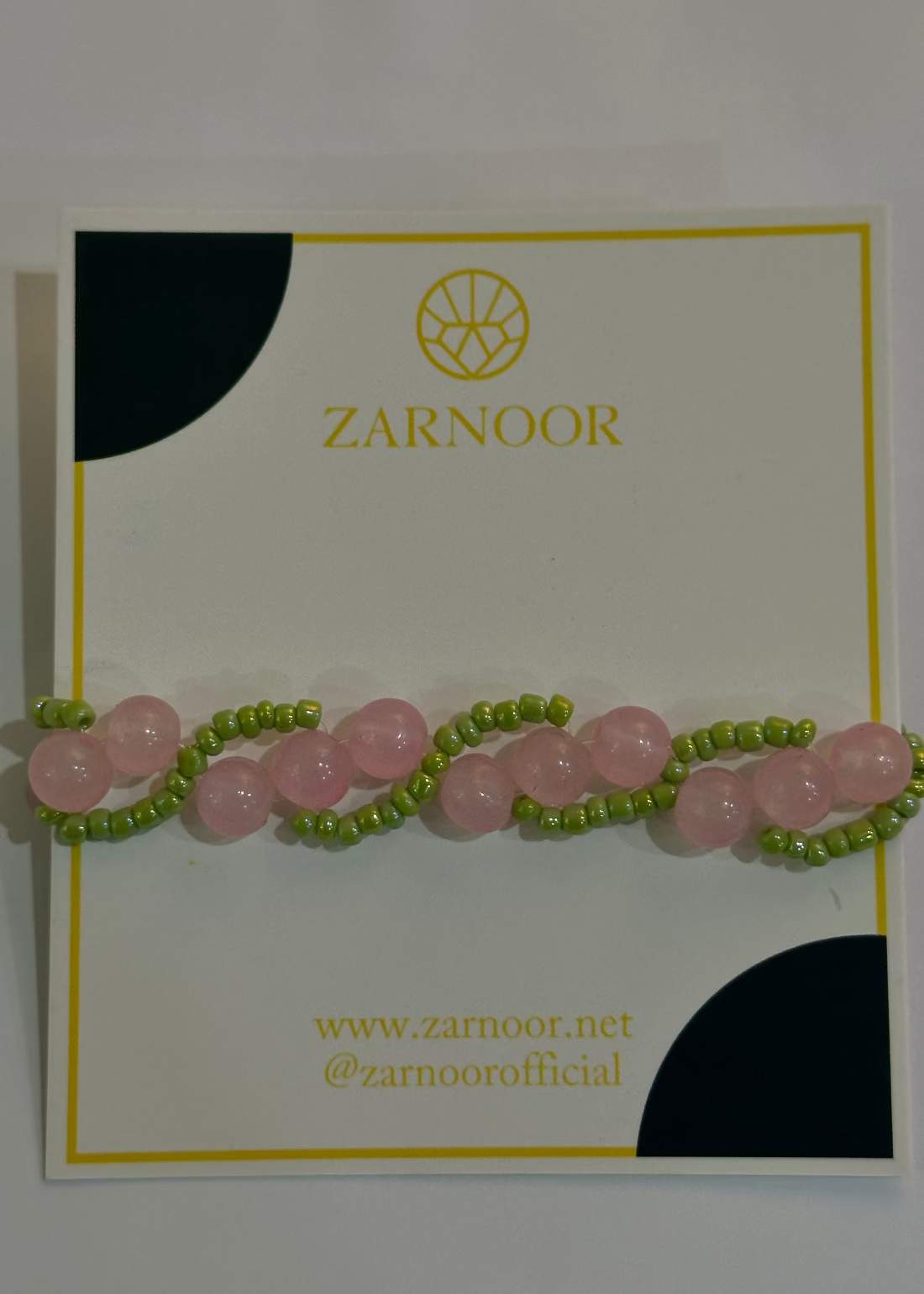 Pink and green beaded bracelet on a Zarnoor branded card.