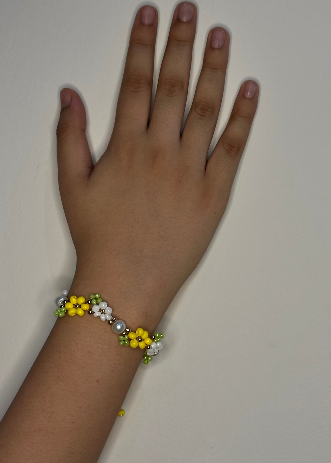 Hand wearing a bracelet with yellow flowers and pearls on a plain background