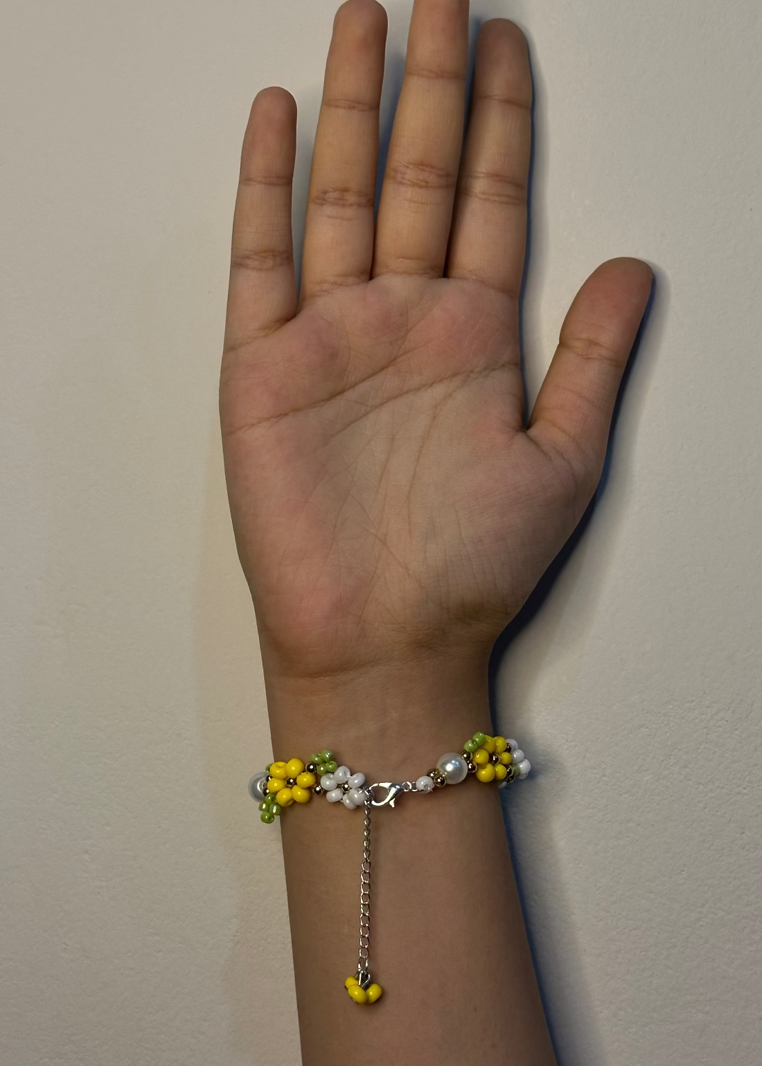 Hand wearing a bracelet with yellow flowers and pearls on a plain background