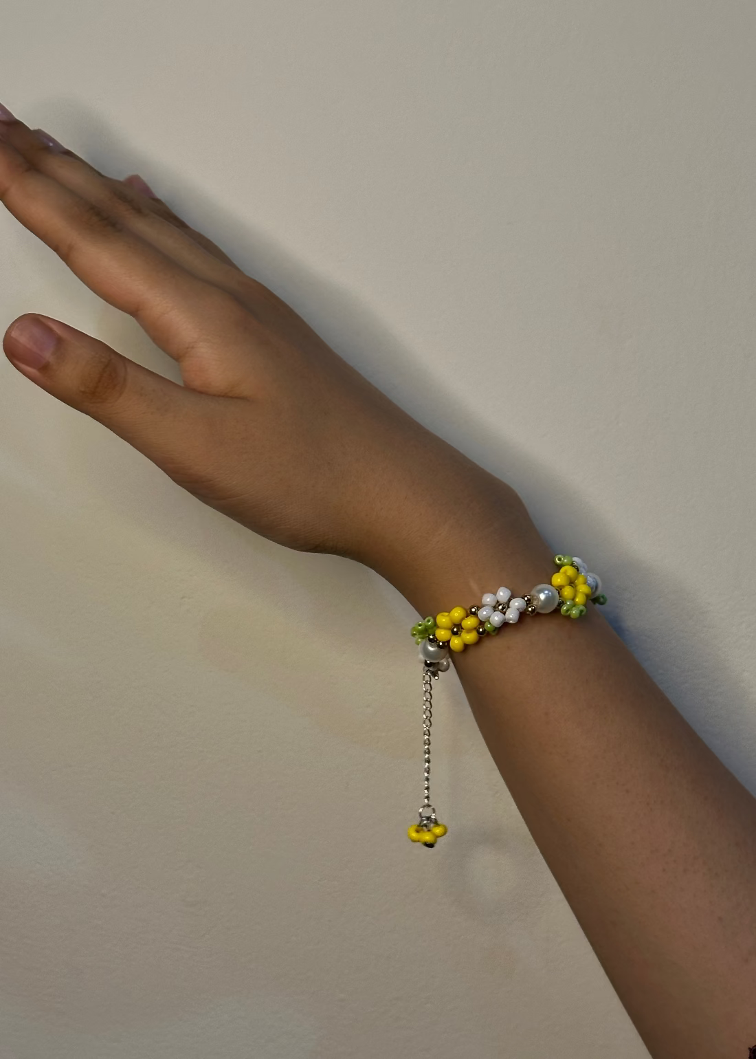 Hand wearing a bracelet with yellow and white beads on a plain background