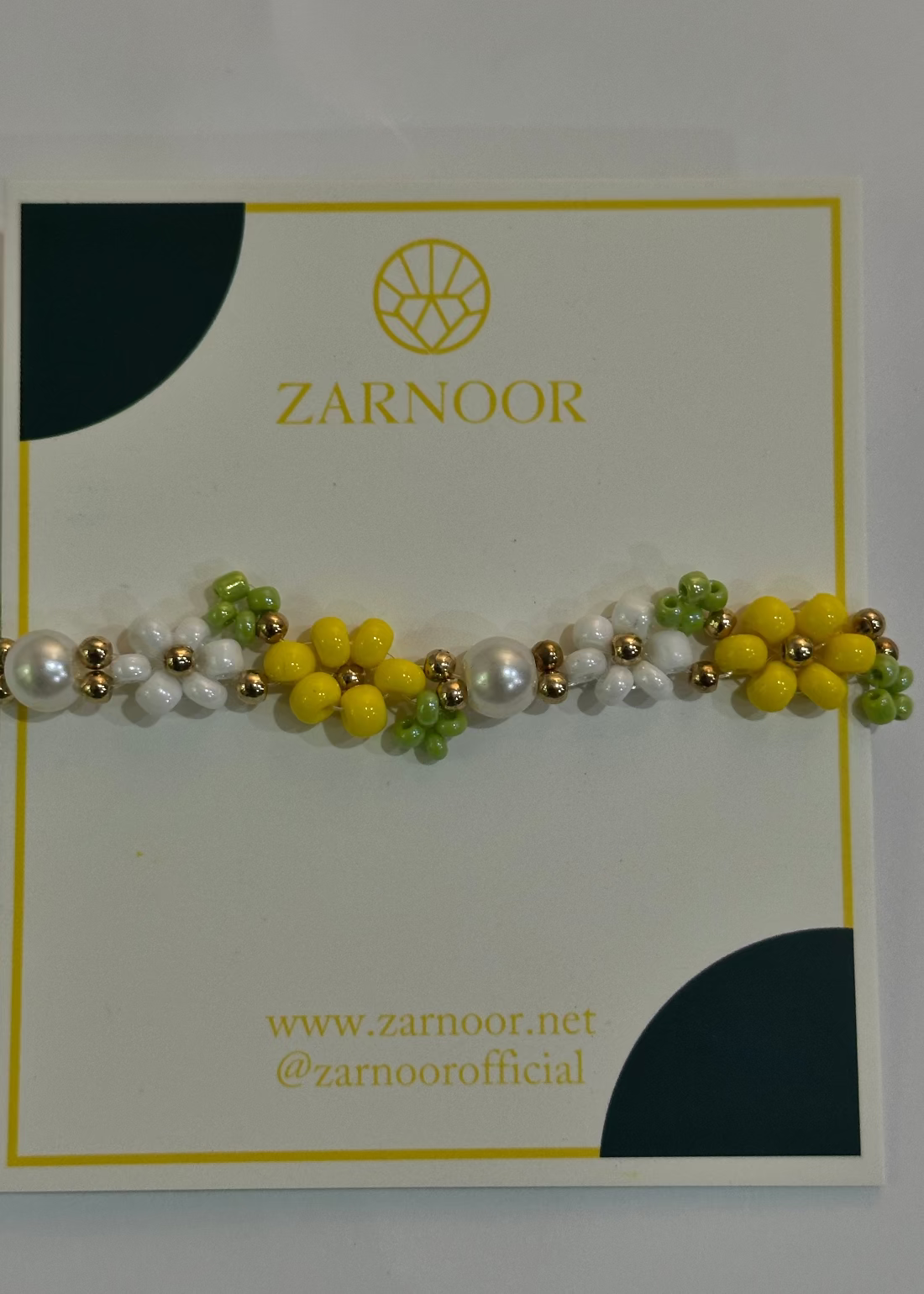 Bracelet with yellow, white, and green beads on a Zarnoor branded card.