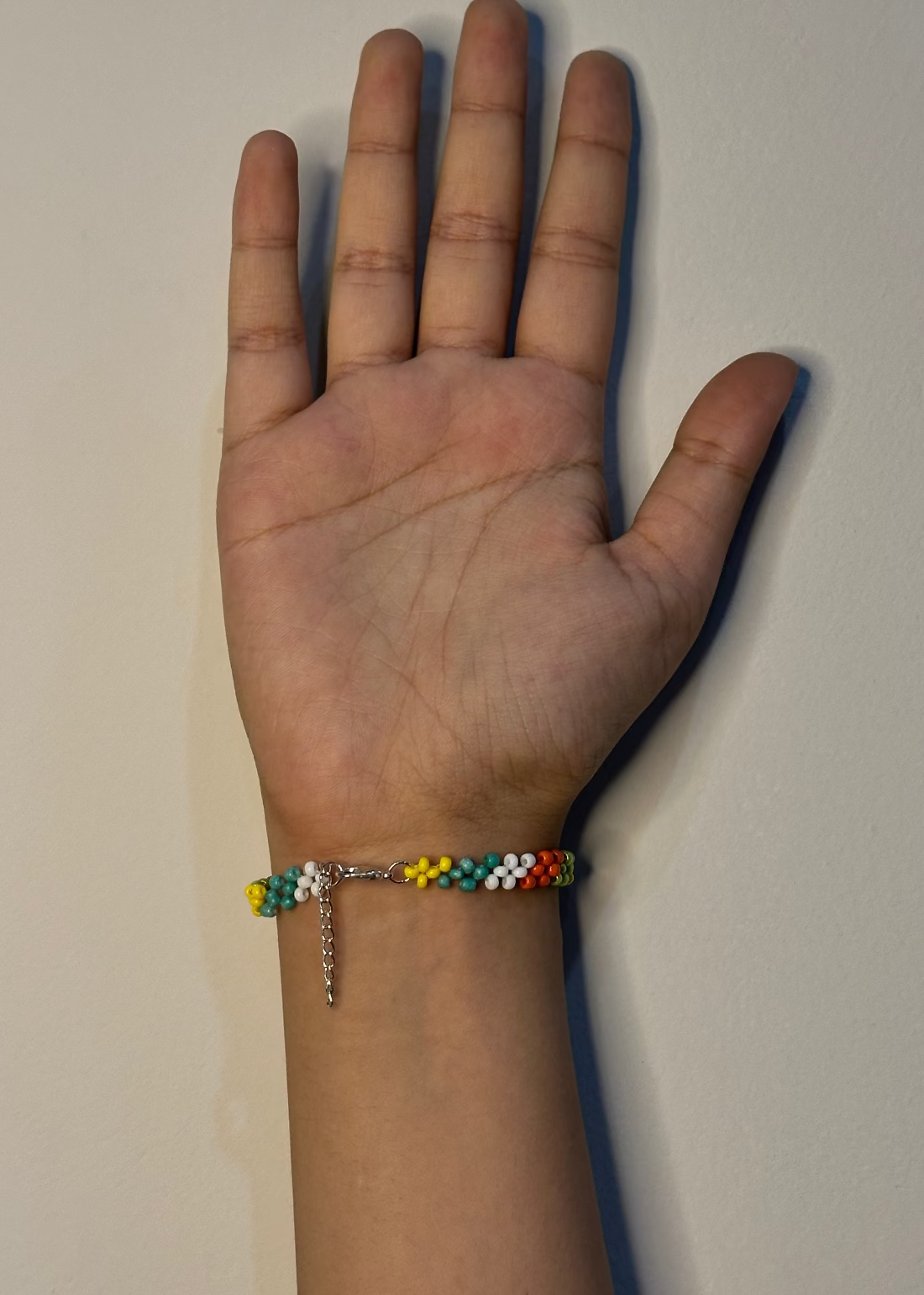Hand wearing a colorful beaded bracelet on a plain background