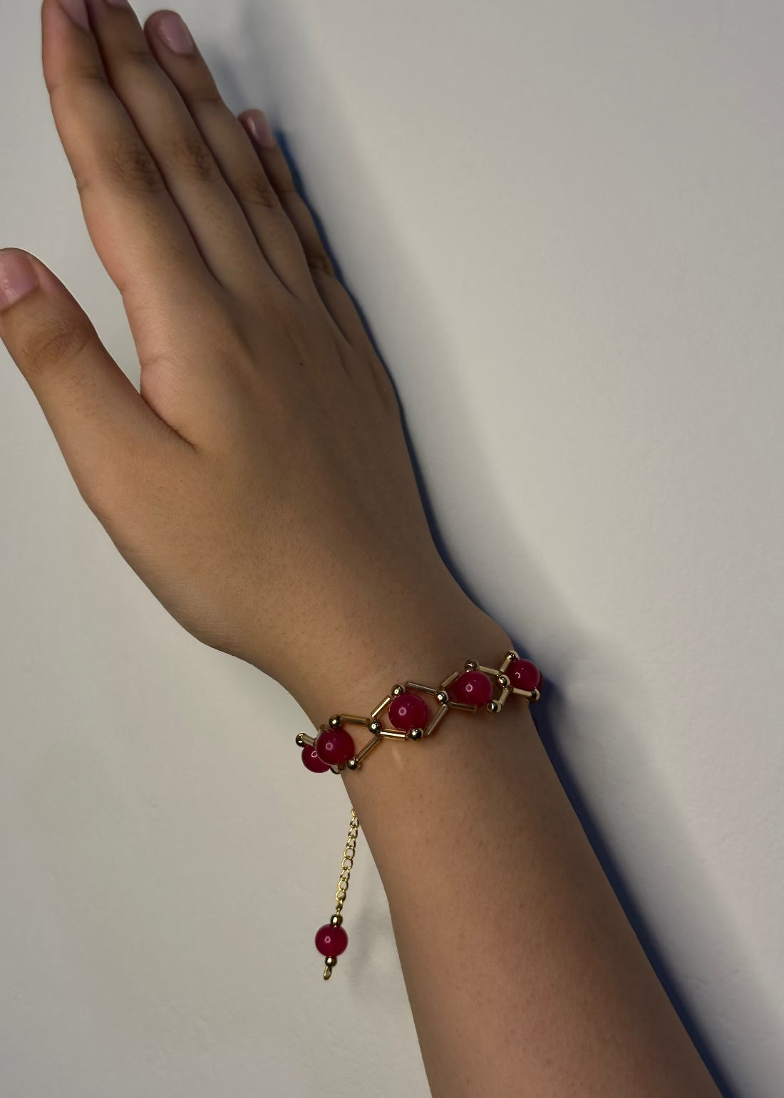 Hand wearing a red beaded bracelet on a plain background