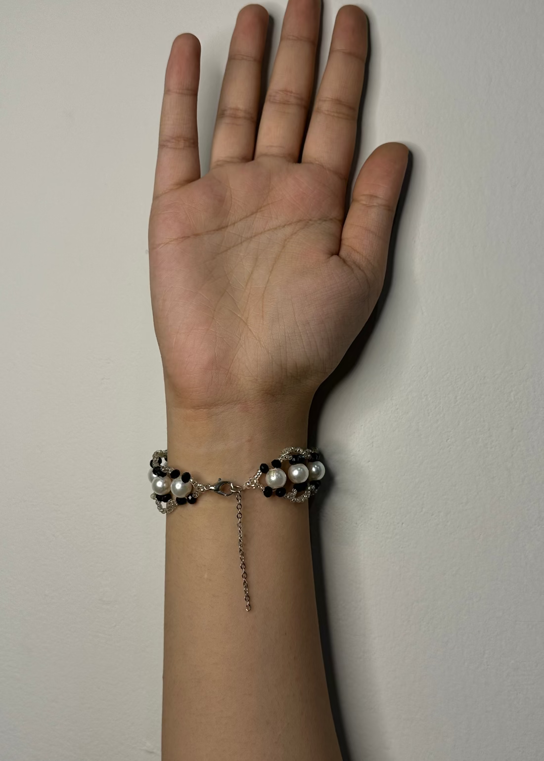 Hand wearing a bracelet with pearls against a plain background