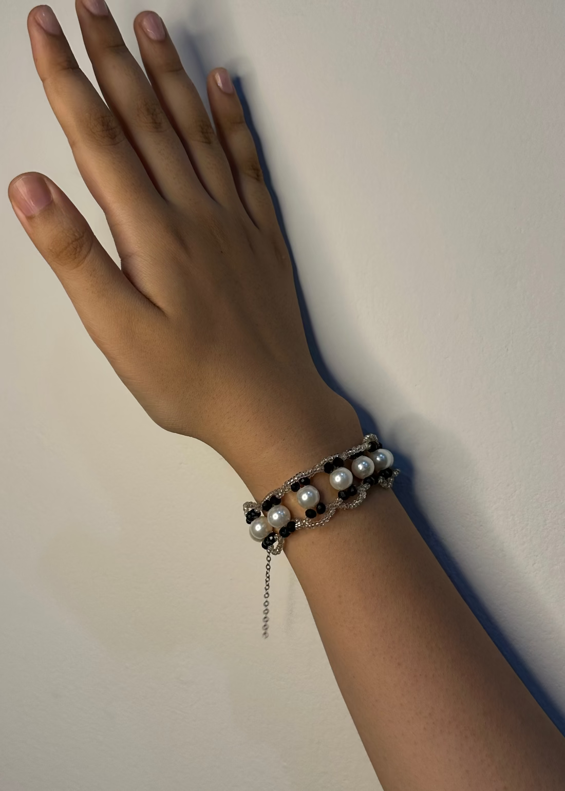 Hand wearing a bracelet with pearls against a plain background