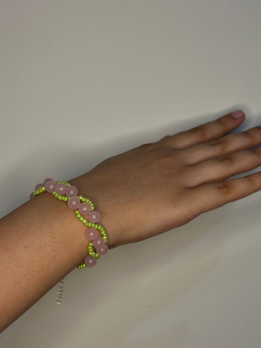 Hand wearing a pink and green beaded bracelet on a plain background
