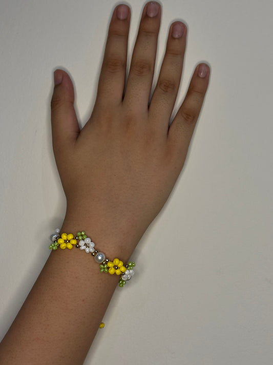 Hand wearing a bracelet with yellow flowers and pearls on a plain background