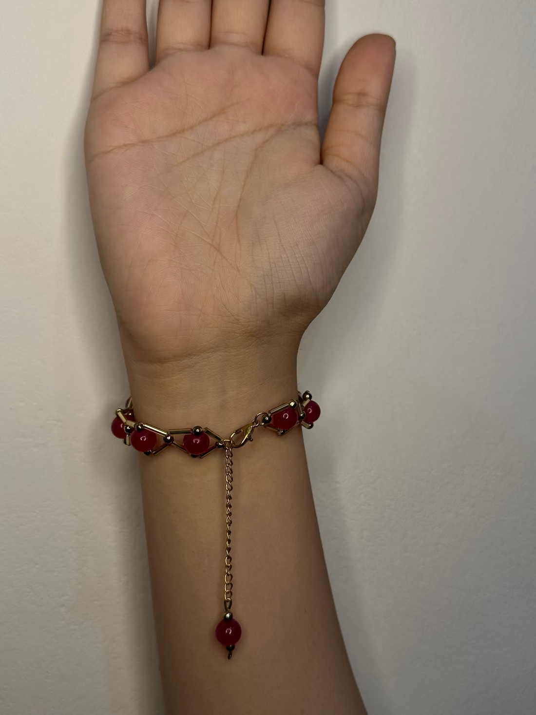 Bracelet with red beads on a wrist against a plain background