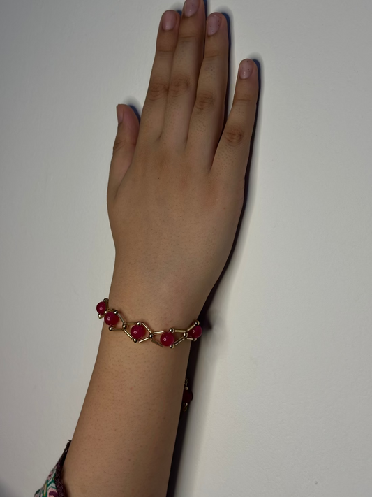 Hand wearing a bracelet with red stones on a plain background